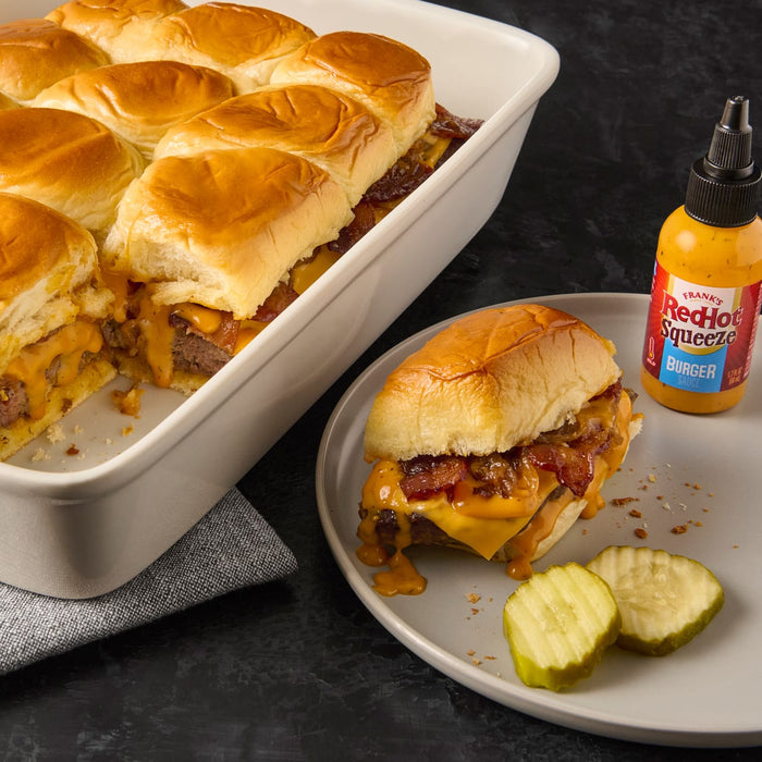 A plate of Franks RedHot Squeeze Burger Sauce with a cheeseburger slider and pickles.