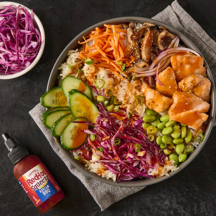 A bowl of rice with salmon edamame red cabbage cucumber carrots mushrooms and Franks RedHot Squeeze Korean BBQ sauce.
