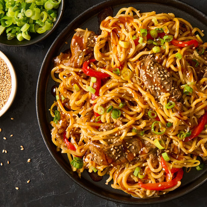 A plate of noodles with beef red peppers and green onions.