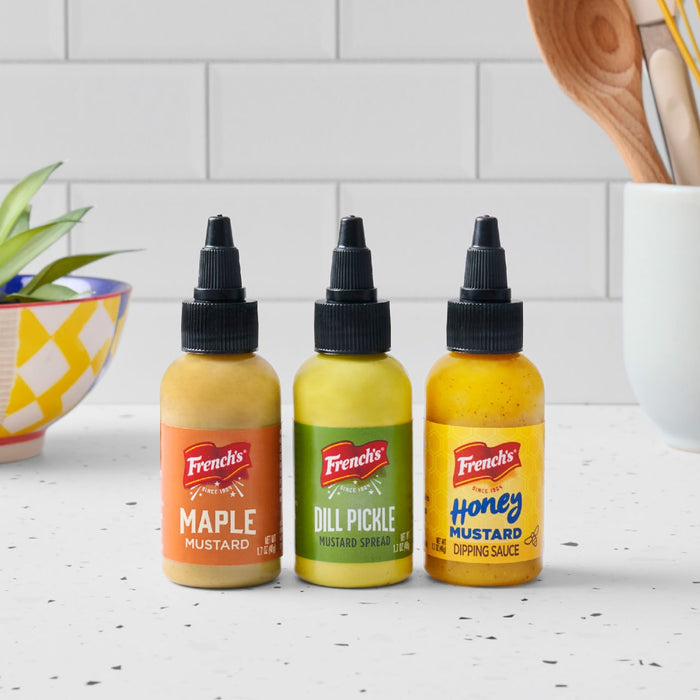 Three bottles of Frenchs mustard in maple dill pickle and honey flavors are displayed on a kitchen counter.