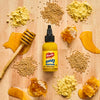 A bottle of Frenchs Honey Mustard Dipping Sauce is surrounded by honey honeycomb mustard seeds and mustard powder on a wooden surface.