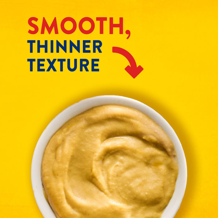A bowl of mustard with a smooth, thinner texture is shown against a yellow background.