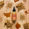 A bottle of French's Maple Mustard is surrounded by piles of brown sugar, mustard seeds, and maple syrup on a wooden surface.