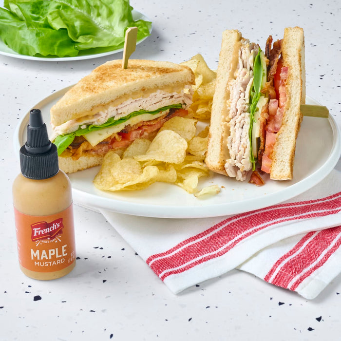 A delicious club sandwich with French's Maple Mustard, chips, and lettuce on a white plate.