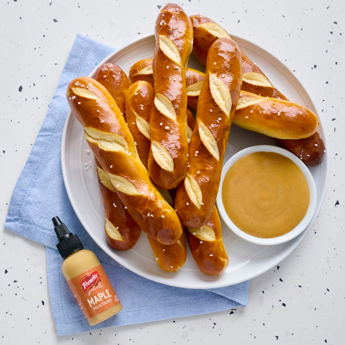 A plate of pretzel sticks with a bowl of dipping sauce and a bottle of French's Maple Mustard.