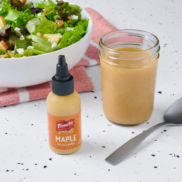 A bottle of French's Maple Mustard and a jar of salad dressing are displayed next to a fresh salad.