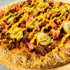 ['A close-up of a pizza with ground beef, pickles, tomatoes, and mustard.']