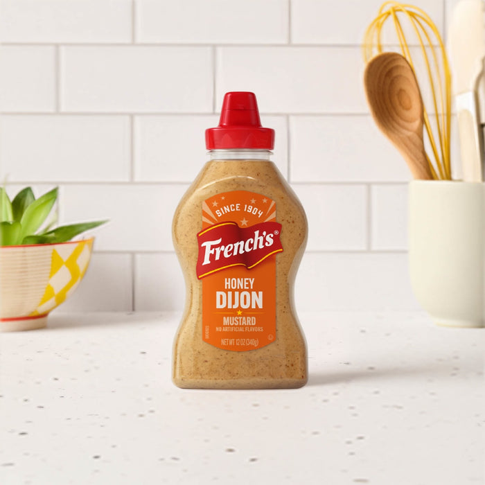 A bottle of Frenchs Brown Honey Dijon Mustard 12 Oz stands on a white speckled countertop in a bright kitchen setting.