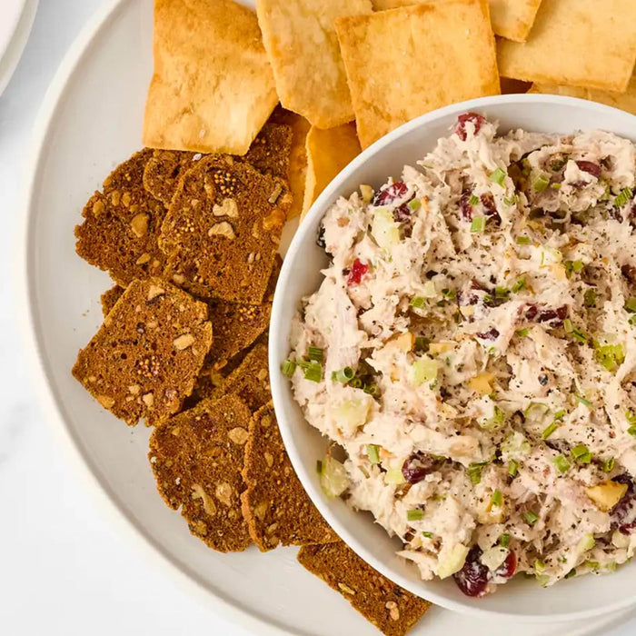 A white bowl filled with creamy chicken salad featuring cranberries and green onions is served alongside pita chips and dark crackers made with Frenchs Brown Honey Dijon Mustard 12 Oz.