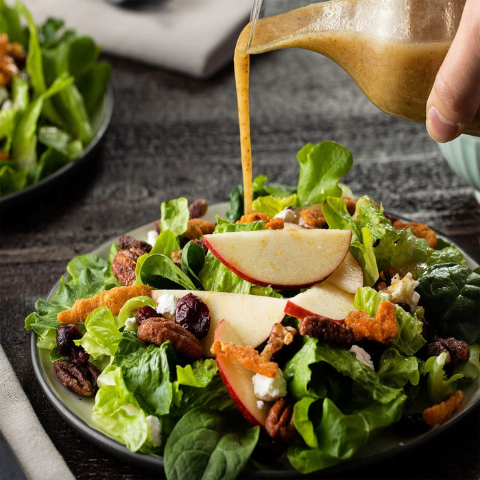 A fresh autumn salad featuring crisp greens, apple slices, pecans, and dried cranberries is drizzled with a savory dressing made from Frenchs Brown Honey Dijon Mustard 12 Oz.
