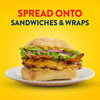 A grilled chicken sandwich with bacon and avocado is layered with Frenchs Brown Honey Dijon Mustard 12 Oz on a white plate against a yellow background.