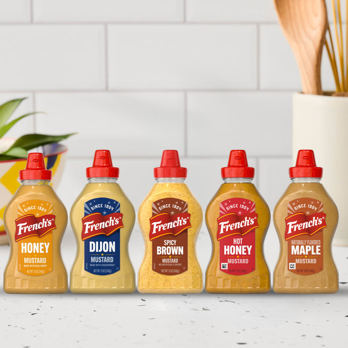 A lineup of five different French's mustard flavors, with the bottle of Frenchs Brown Spicy Brown Mustard 12 Oz in the center, is displayed on a kitchen counter to showcase the brand's variety.