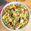 A bowl of creamy macaroni salad with hard-boiled eggs, peas, and tomatoes is shown, made with a flavorful dressing using Frenchs Brown Spicy Brown Mustard 12 Oz.