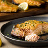 A flaky, cooked salmon fillet is shown on a dark plate, glazed with a delicious sauce made using Frenchs Brown Spicy Brown Mustard 12 Oz.