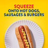 A hot dog in a bun on a paper plate is topped with a zigzag of Frenchs Brown Spicy Brown Mustard 12 Oz, with text above that reads, SQUEEZE ONTO HOT DOGS, SAUSAGES &amp; BURGERS.