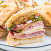 A close-up of a large Italian-style sandwich cut into wedges, revealing layers of deli meats, cheese, vegetables, and a tangy spread made with Frenchs Brown Honey Mustard 12 Oz.
