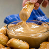A hand dips a pretzel into a bowl of cheese sauce.