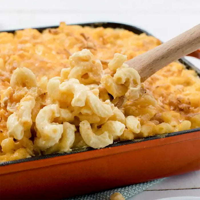 A wooden spoon scoops up a serving of creamy baked macaroni and cheese, a delicious recipe that can be made with Frenchs Beige Dijon Chardonnay Mustard 12 Oz.
