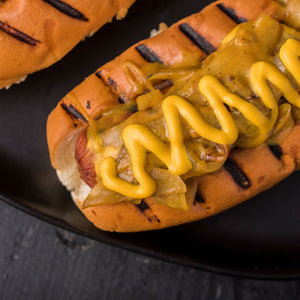 ['A close-up of a hot dog with mustard and onions on a bun.']