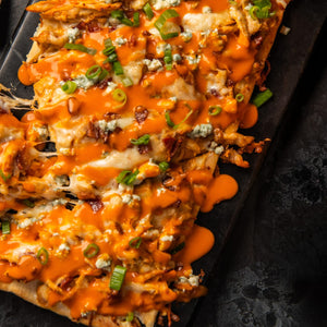 A buffalo chicken flatbread is generously drizzled with Franks Red Hot Regular Wing Hot Sauce Mild 12 Oz and topped with melted cheese, blue cheese crumbles, and fresh green onions.