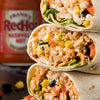A stack of three chicken burritos filled with rice, corn, and black beans sits in front of a bottle of Franks Red Hot Regular Wing Hot Sauce Hot 12 Oz.