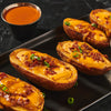 ['Baked potato skins topped with cheese, bacon, and chives on a black plate.']
