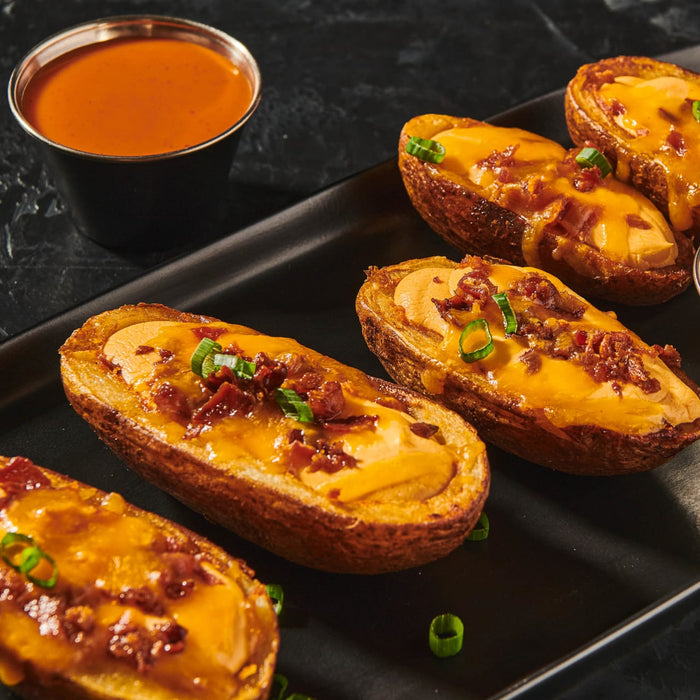 ['Baked potato skins topped with cheese, bacon, and chives on a black plate.']