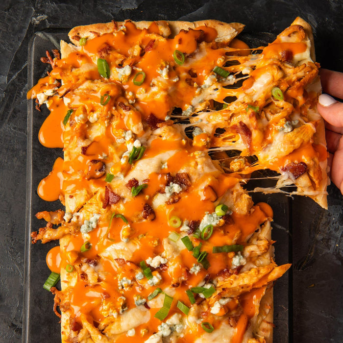 ['A close-up of a buffalo chicken pizza with melted cheese and green onions.']