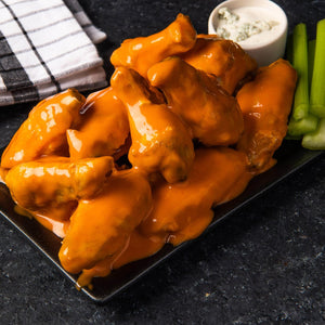 ['A plate of chicken wings covered in orange sauce with celery sticks and blue cheese dip.']