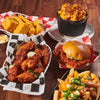 ['A table with a variety of food items, including chicken wings, a sandwich, fries, and cornbread.']