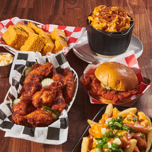 ['A table with a variety of food items, including chicken wings, a sandwich, fries, and cornbread.']