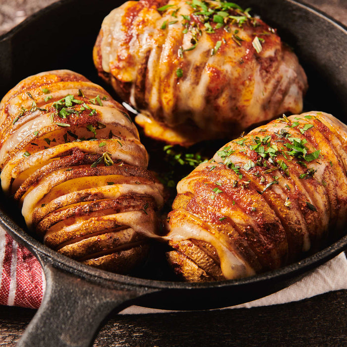 ['Three baked potatoes with cheese and herbs in a cast iron skillet.']