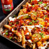 ["A close-up of a plate of loaded fries with Frank's RedHot sauce, bacon, cheese, and pickles."]