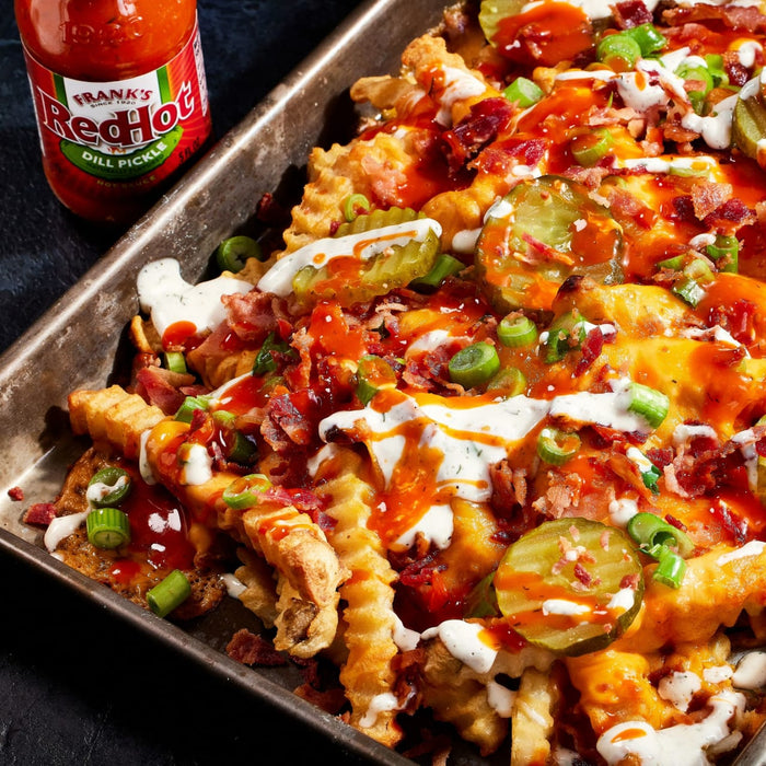 ["A close-up of a plate of loaded fries with Frank's RedHot sauce, bacon, cheese, and pickles."]