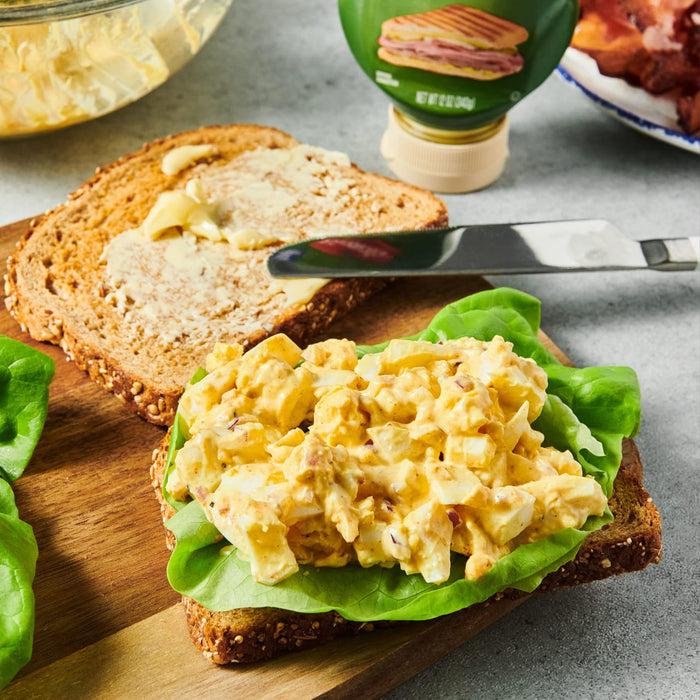 ['A sandwich with egg salad on a bed of lettuce on a wooden cutting board.']
