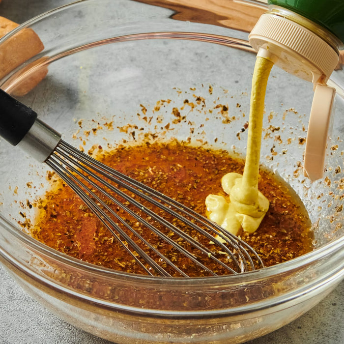 ['A glass bowl with a whisk, mustard, and spices inside.']