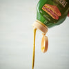['A bottle of pickle mustard spread is being squeezed, with the mustard coming out of the bottle.']