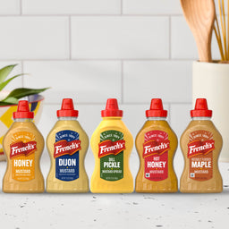 The Frenchs Dill Pickle Sandwich Spread Regular Inverted Squeeze Bottle Rp 12 Oz is featured in the center of a lineup of five different French's mustards, showcasing the variety of flavors available.