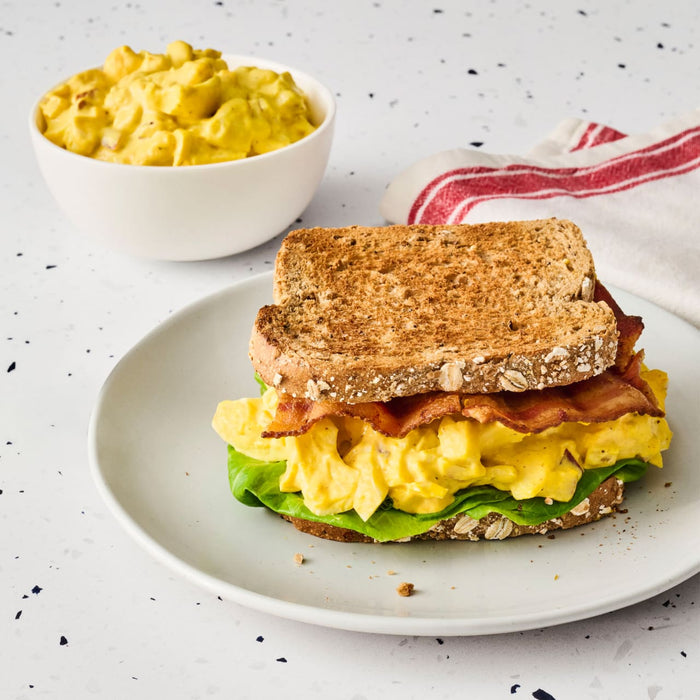 A bacon and salad sandwich on toasted whole wheat bread, featuring a creamy filling made with Frenchs Dill Pickle Sandwich Spread Regular Inverted Squeeze Bottle Rp 12 Oz, is presented on a plate.
