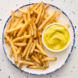 A top-down view of a plate of crispy french fries served with a small bowl of Frenchs Dill Pickle Sandwich Spread Regular Inverted Squeeze Bottle Rp 12 Oz for dipping.