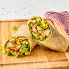 A delicious chicken wrap, cut in half to show the fillings, is made with Frenchs Dill Pickle Sandwich Spread Regular Inverted Squeeze Bottle Rp 12 Oz and served on a wooden board.