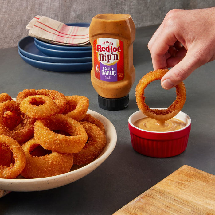 ["A hand dips a crispy onion ring into a bowl of Frank's RedHot Dip'n Roasted Garlic Sauce."]