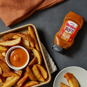 ["A bowl of dipping sauce next to a plate of potato wedges and a bottle of Frank's RedHot Dip'n Golden Sauce."]