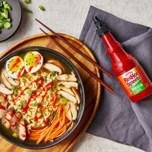["A bowl of ramen with a side of Frank's RedHot Squeeze Sriracha Sauce."]