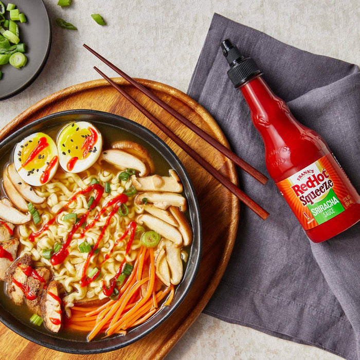 ["A bowl of ramen with a side of Frank's RedHot Squeeze Sriracha Sauce."]