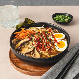 ['A bowl of ramen with mushrooms, bean sprouts, carrots, and two eggs.']