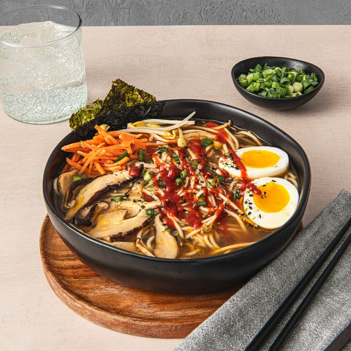 ['A bowl of ramen with mushrooms, bean sprouts, carrots, and two eggs.']