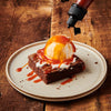 ['A brownie topped with ice cream and caramel sauce is drizzled with more caramel sauce.']
