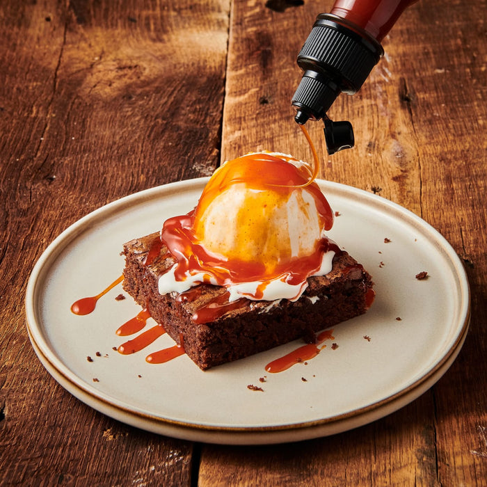 ['A brownie topped with ice cream and caramel sauce is drizzled with more caramel sauce.']