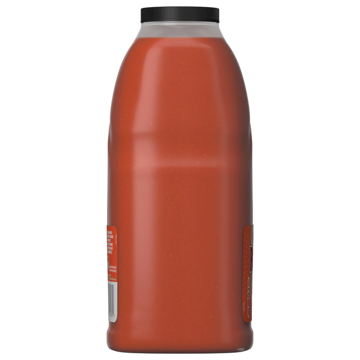 A side view of a large bottle of Franks Red Hot Mango Habanero Wing Hot Sauce Regular 64 Oz, showing the reddish-orange sauce inside the clear container.